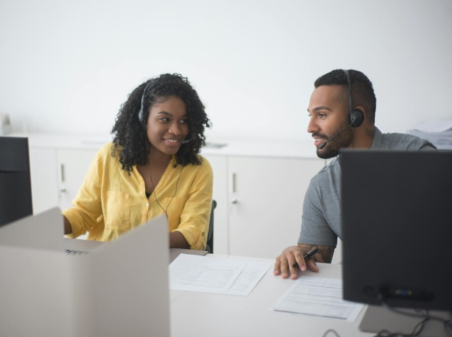 Woman in Yellow Dress Up Shirt with Headset Consulting to a Man Beside Her at Work